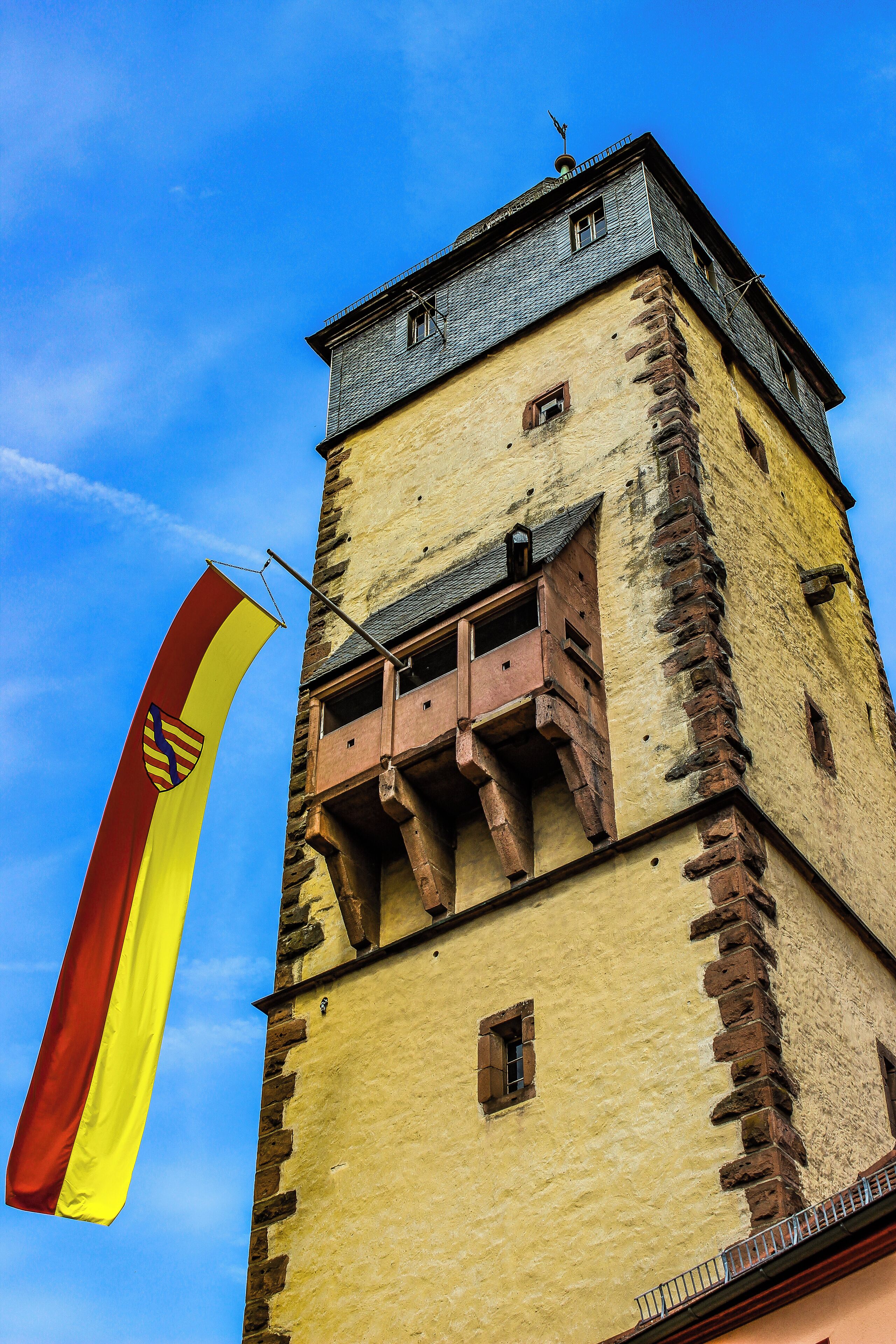 A historic tower with a flag, stone facade, and a small balcony.