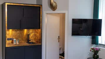 A hotel room with a bed, a minibar, a television, and a chandelier.