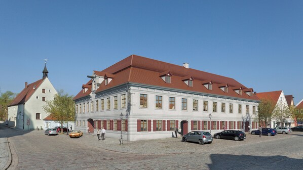 A historic building with a red-tiled roof, large windows, and a prominent corner tower.