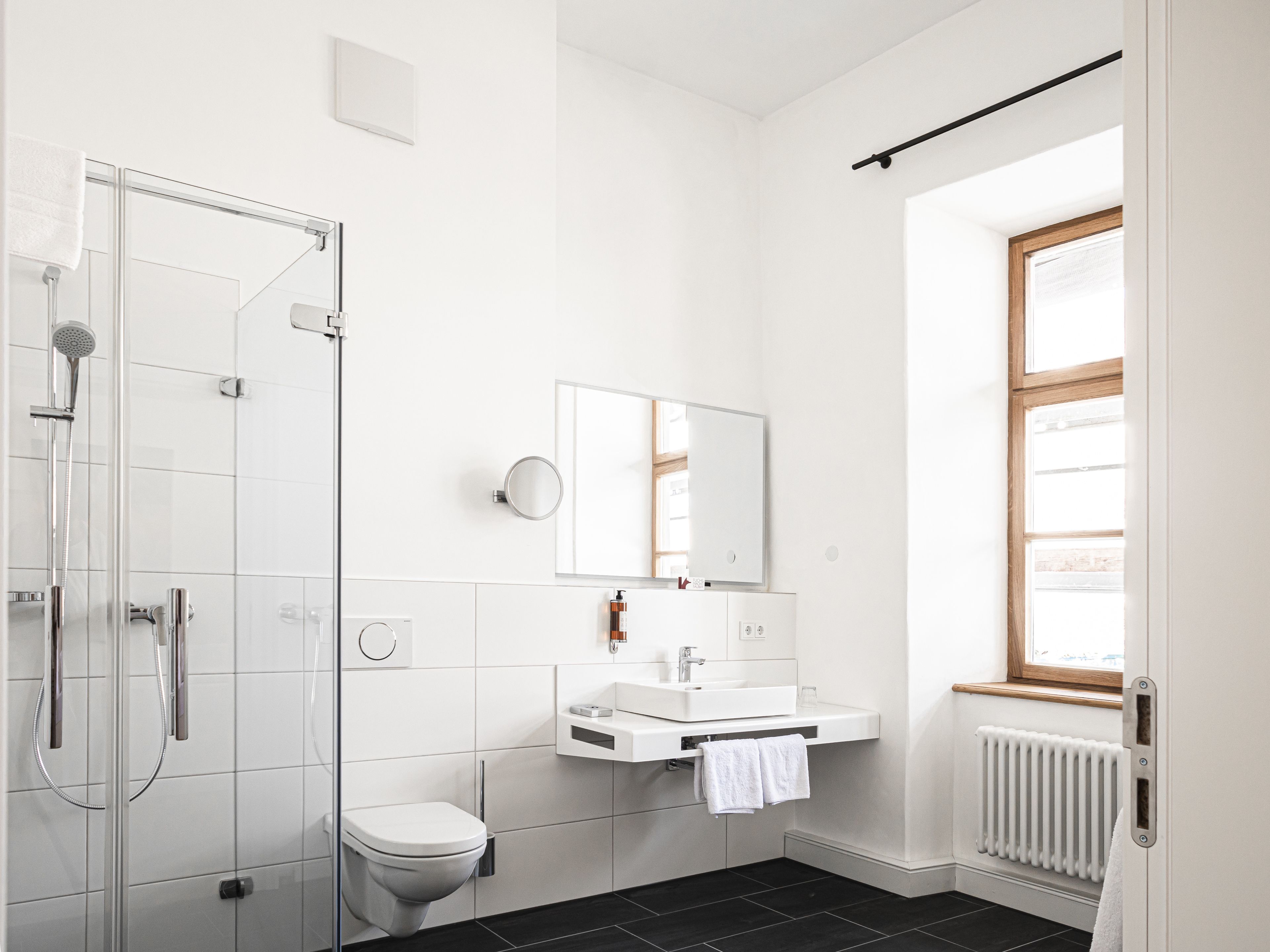 Un baño moderno con cabina de ducha de vidrio, inodoro blanco, lavabo con espejo y ventana que proporciona luz natural.