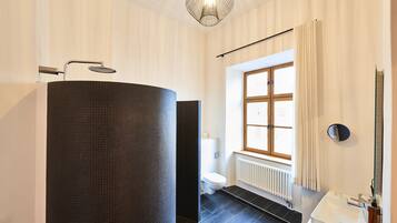 A modern bathroom with a large dark tiled sink, a white toilet, and a window with curtains.