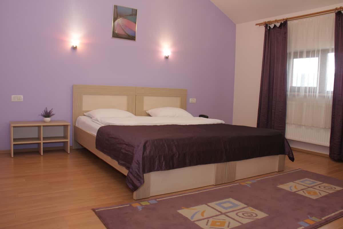 Une chambre à coucher avec un lit, des tables de chevet, une petite table, une plante en pot et une fenêtre avec des rideaux.