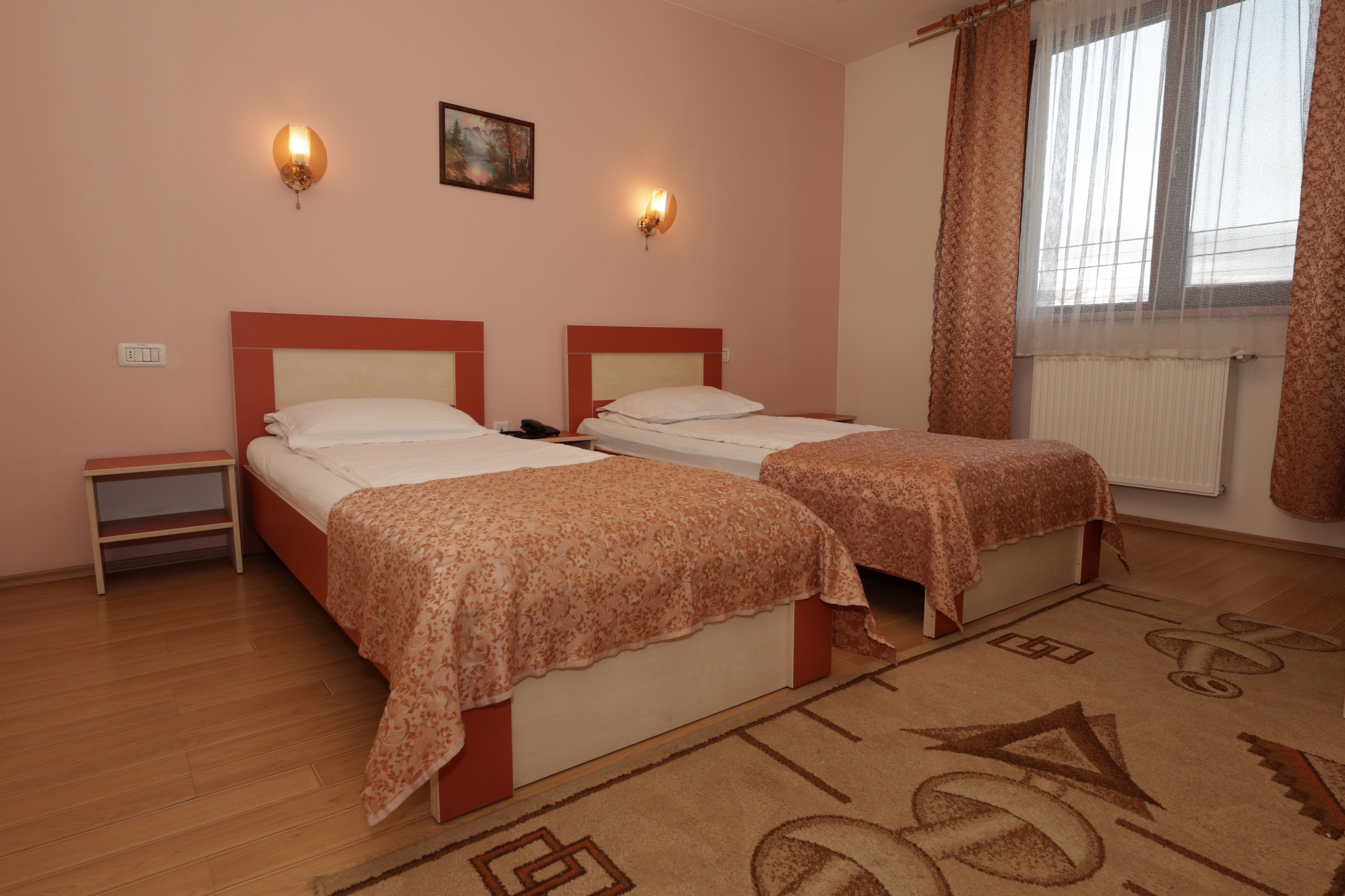 A hotel room with two beds, a nightstand, a painting on the wall, and a window with curtains.