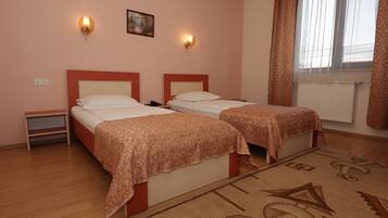 A hotel room with two beds, a nightstand, a painting on the wall, and a window with curtains.