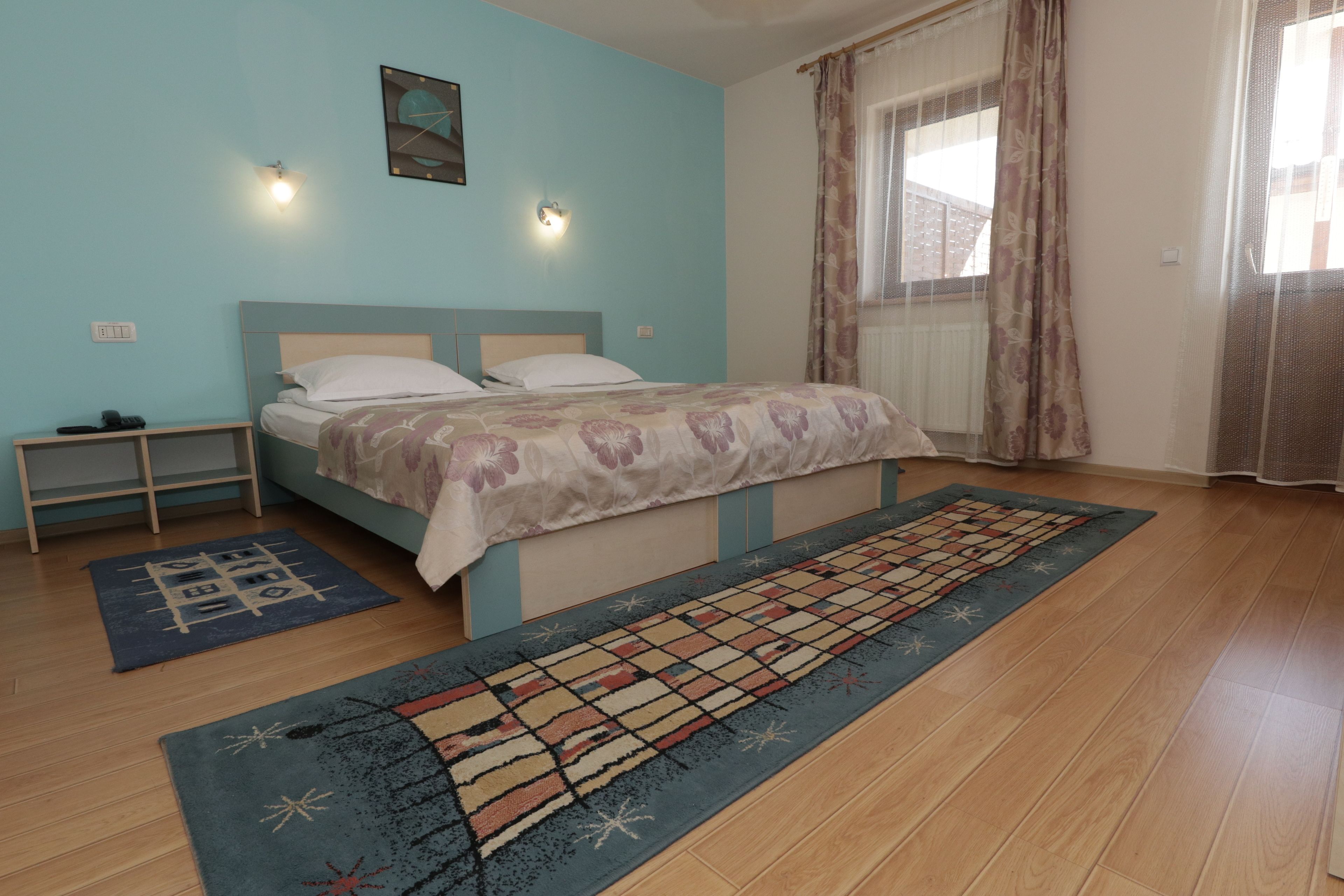 A bedroom with a bed, a nightstand, a window with curtains, and a patterned rug.