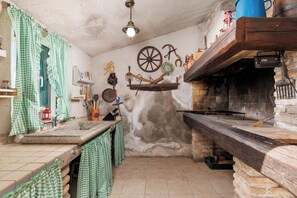 A rustic kitchen with a stone wall, a wooden counter, and various kitchen utensils hanging on the wall. - Villa with pool and private waterfront (Jablanac)