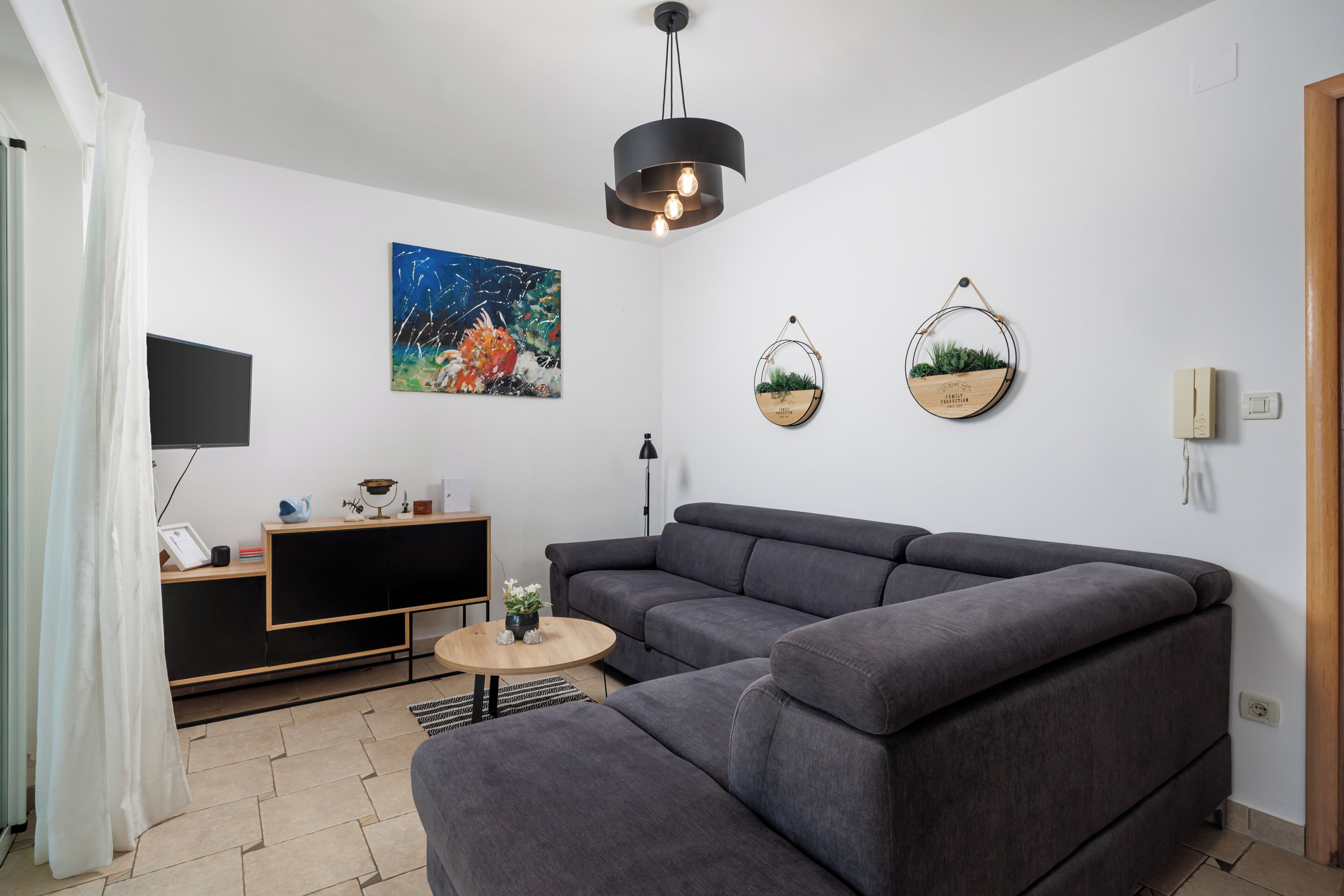 Uma sala de estar moderna com um sofá modular, uma televisão de tela plana, um quadro e dois vasos de plantas fixados na parede.