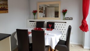 Uma sala de jantar com uma mesa posta para dois, um espelho sobre a mesa e um letreiro na parede com a inscrição 'HOME SWEET HOME'.