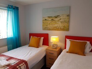 A hotel room with two beds, a red headboard, a bedside lamp, a painting on the wall, and a window with blue curtains. - Penllech House - Huku Kwetu (Nottingham)