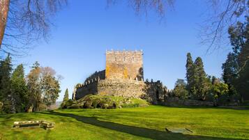 Un château historique en pierre, doté d’une tour centrale, entouré d’une pelouse bien entretenue et d’arbres.