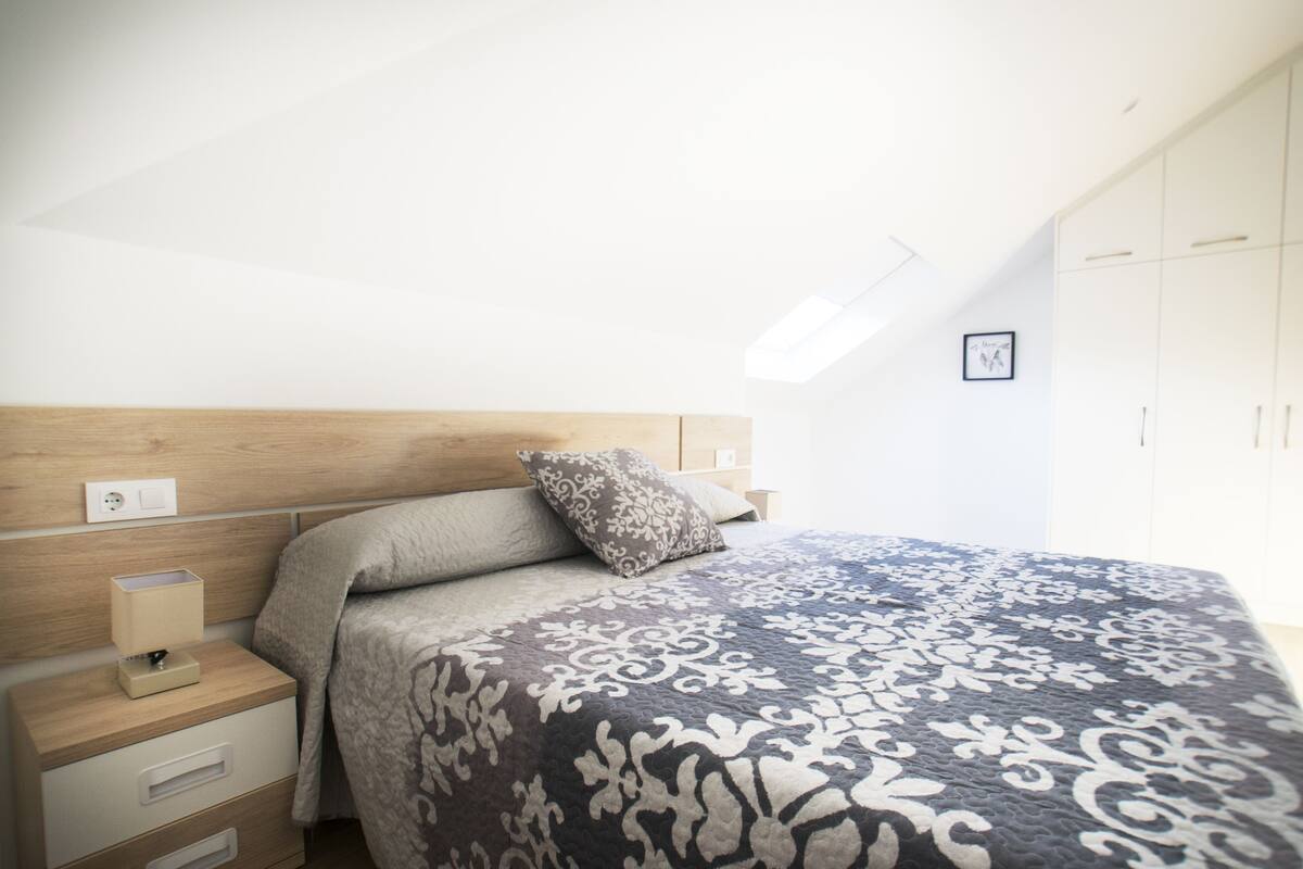 Ein Schlafzimmer mit einem hölzernen Kopfende, einem Nachttisch mit Schubladen, einer gemusterten Bettdecke und einem Kleiderschrank mit Türen.