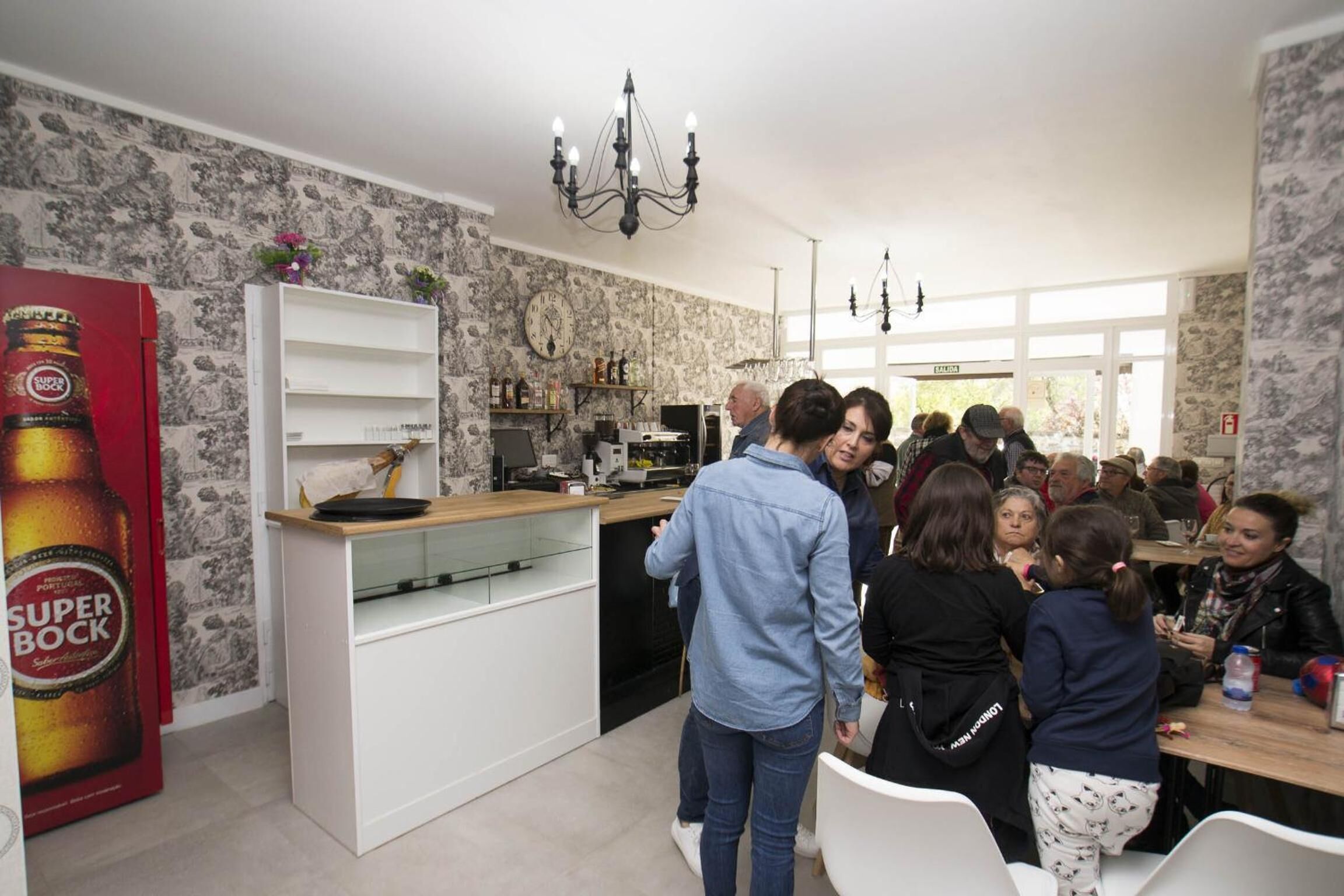 Una cocina moderna con muebles blancos, una araña y un gran anuncio de cerveza Super Bock.
