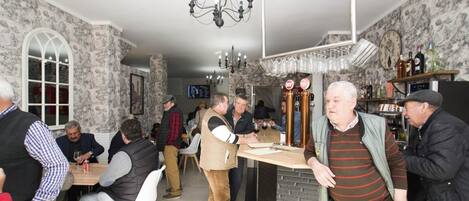 A social gathering in a room with patterned wallpaper, a chandelier, and a bar area with glasses and bottles.