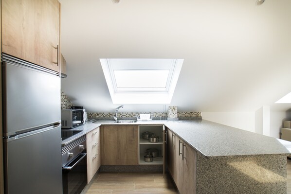 A modern kitchen with a skylight, stainless steel appliances, and wooden cabinetry. - Hostel Albergue O Meson - Apartamentos (Pontevedra)