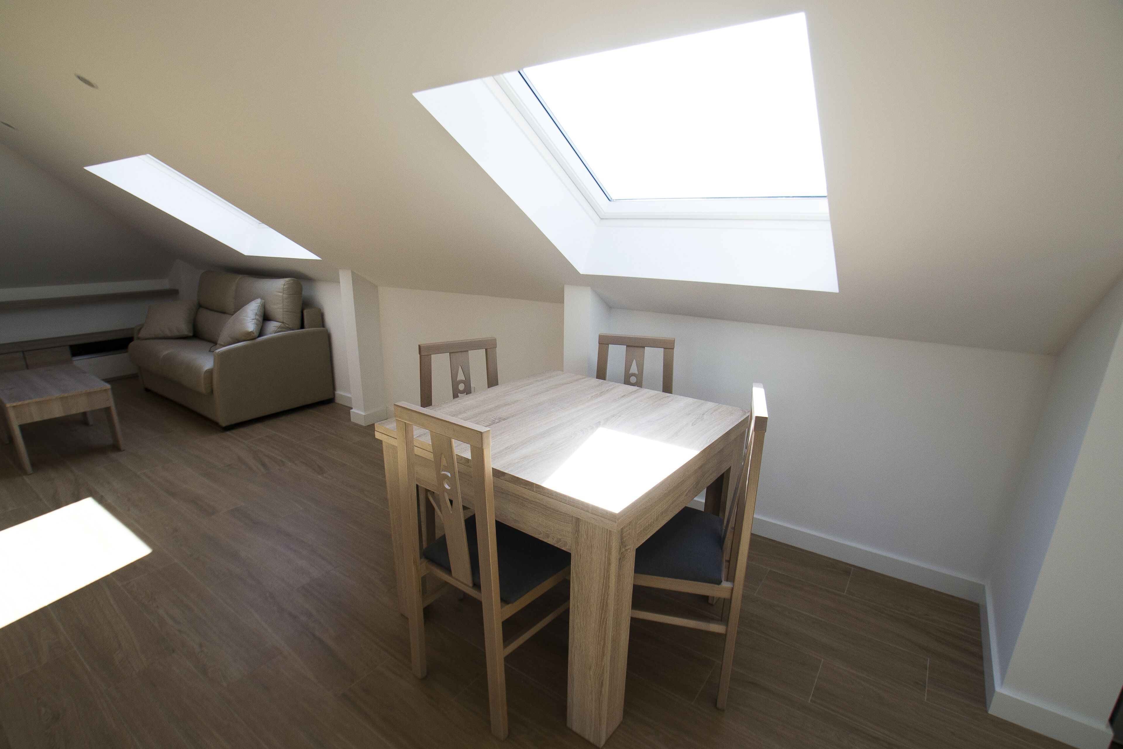 A room with a skylight, a dining table with chairs, and a sofa.