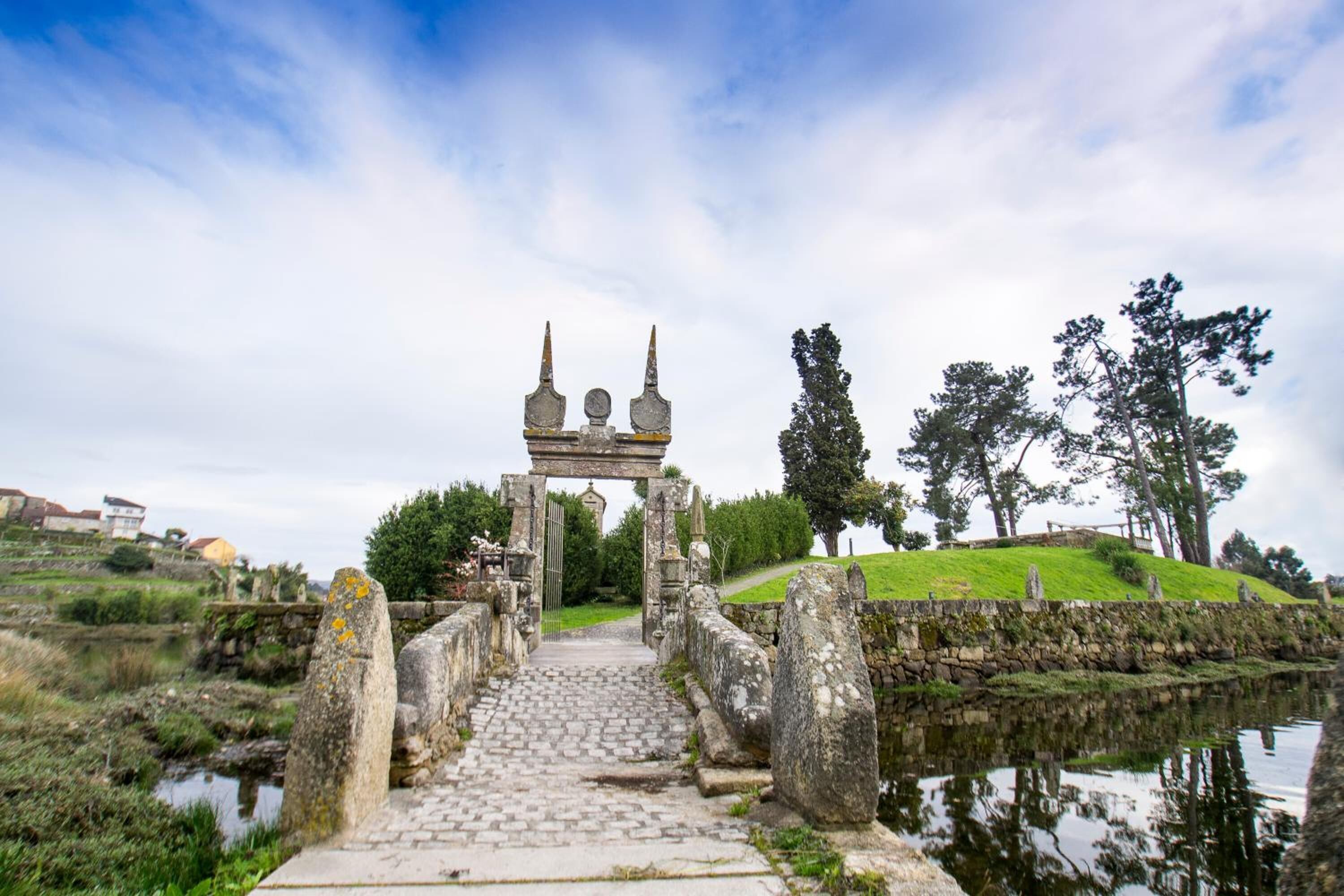 A stone pathway leading to a traditional stone archway with a small bridge over a body of water.