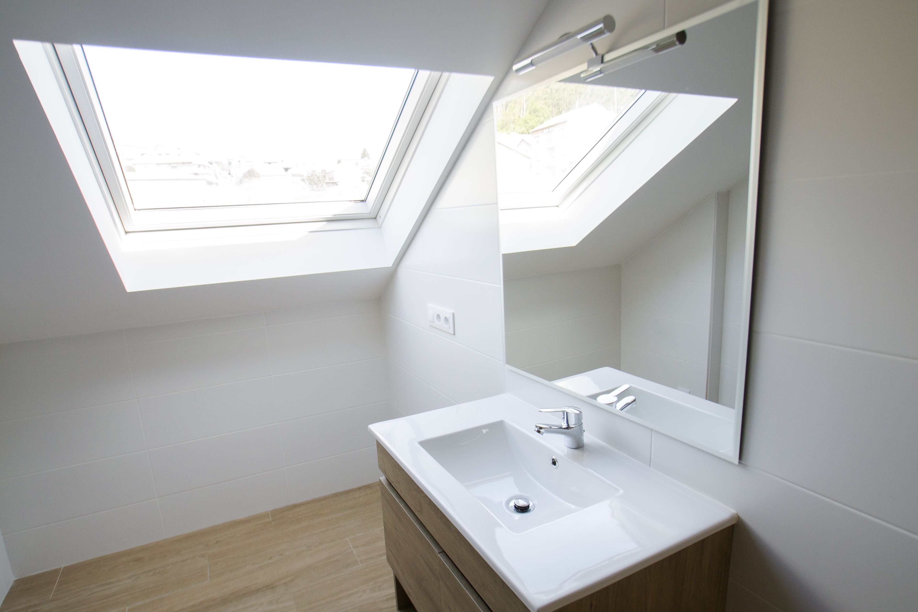 Un baño moderno con tragaluces, un lavamanos blanco y un mueble de tocador de madera.