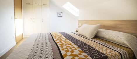 Un dormitorio con techo inclinado, tragaluz, cama con ropa de cama estampada y armario.