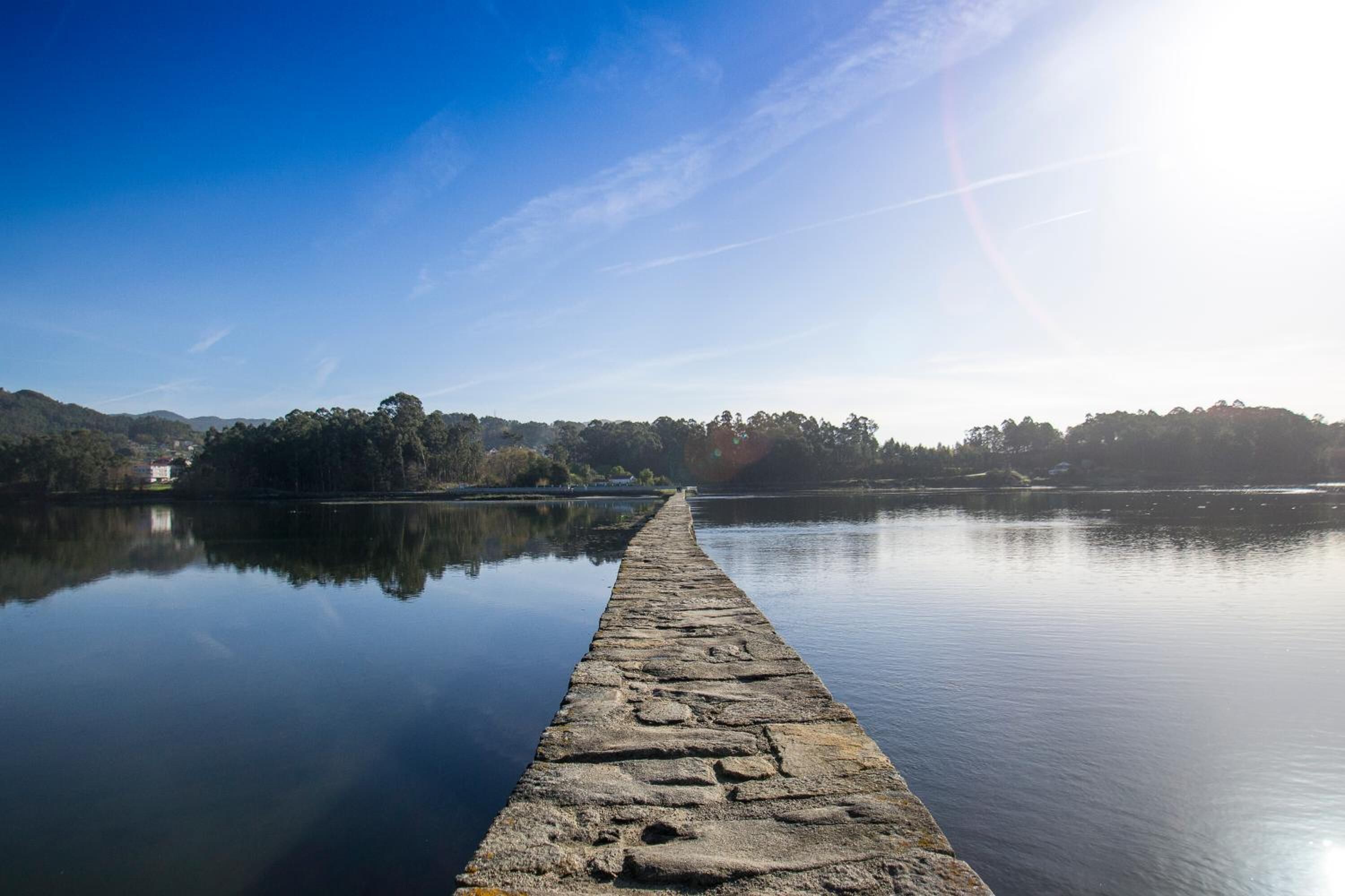 A stone pier extending into calm water, surrounded by trees and hills.