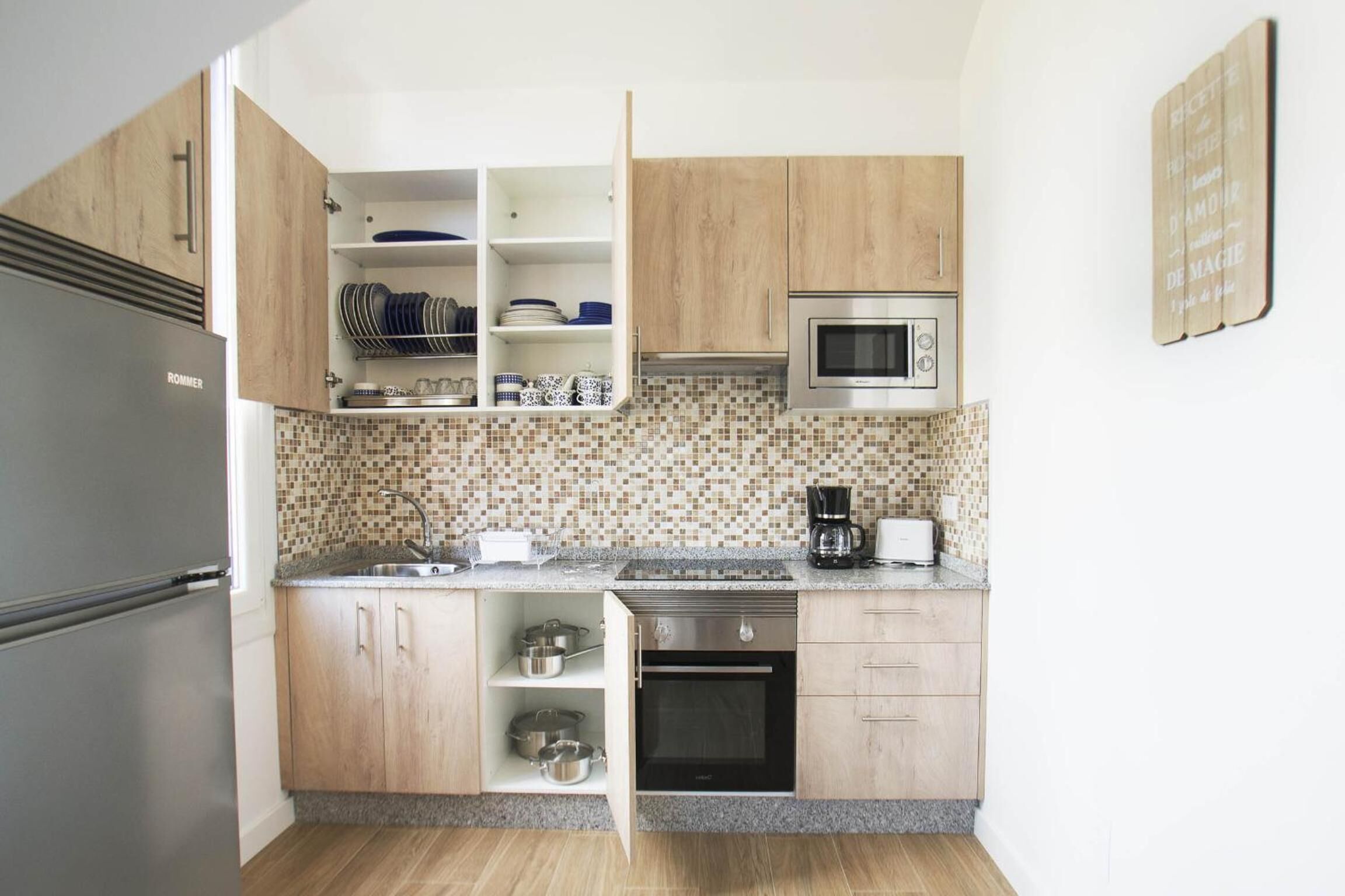 Una cocina compacta con armarios de madera, microondas integrado, cafetera y refrigerador.