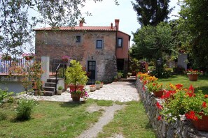 A stone house with a red-tiled roof, a stone pathway, and a garden with potted plants and flowers.