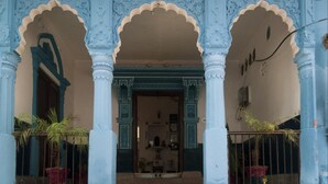 Un bâtiment orné d’arches et de colonnes décoratives, un escalier menant à l’entrée et des plantes en pot.