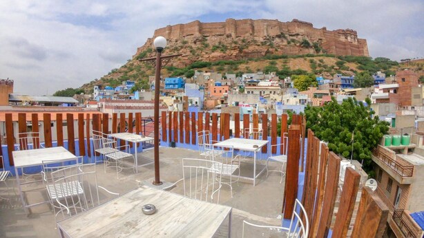 Une terrasse sur le toit, aménagée avec des tables et des chaises, d’où l’on peut admirer une ville aux bâtiments colorés et une colline imposante en arrière-plan.