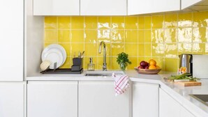 Una cocina con armarios blancos, un salpicadero amarillo, un fregadero y un bol de fruta sobre la encimera.