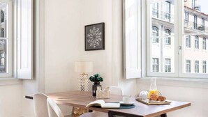 Un comedor con una mesa de madera, sillas blancas, un cuadro en la pared y una ventana con vistas a la ciudad.
