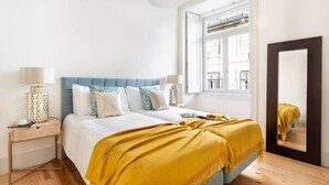 Un dormitorio con cama, mesitas de noche, ventana y espejo.