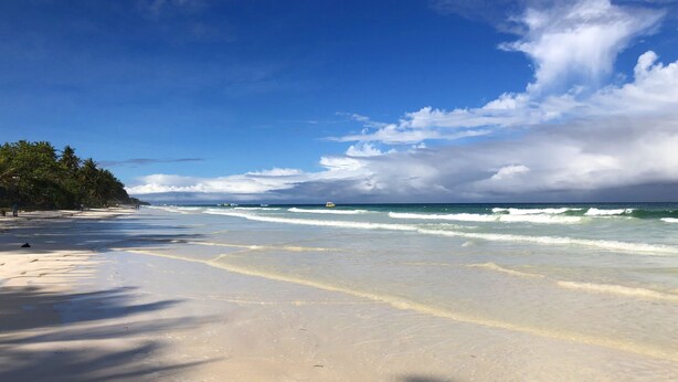 Ein Strand mit blauem Himmel, sanften Wellen und einem sandigen Ufer.