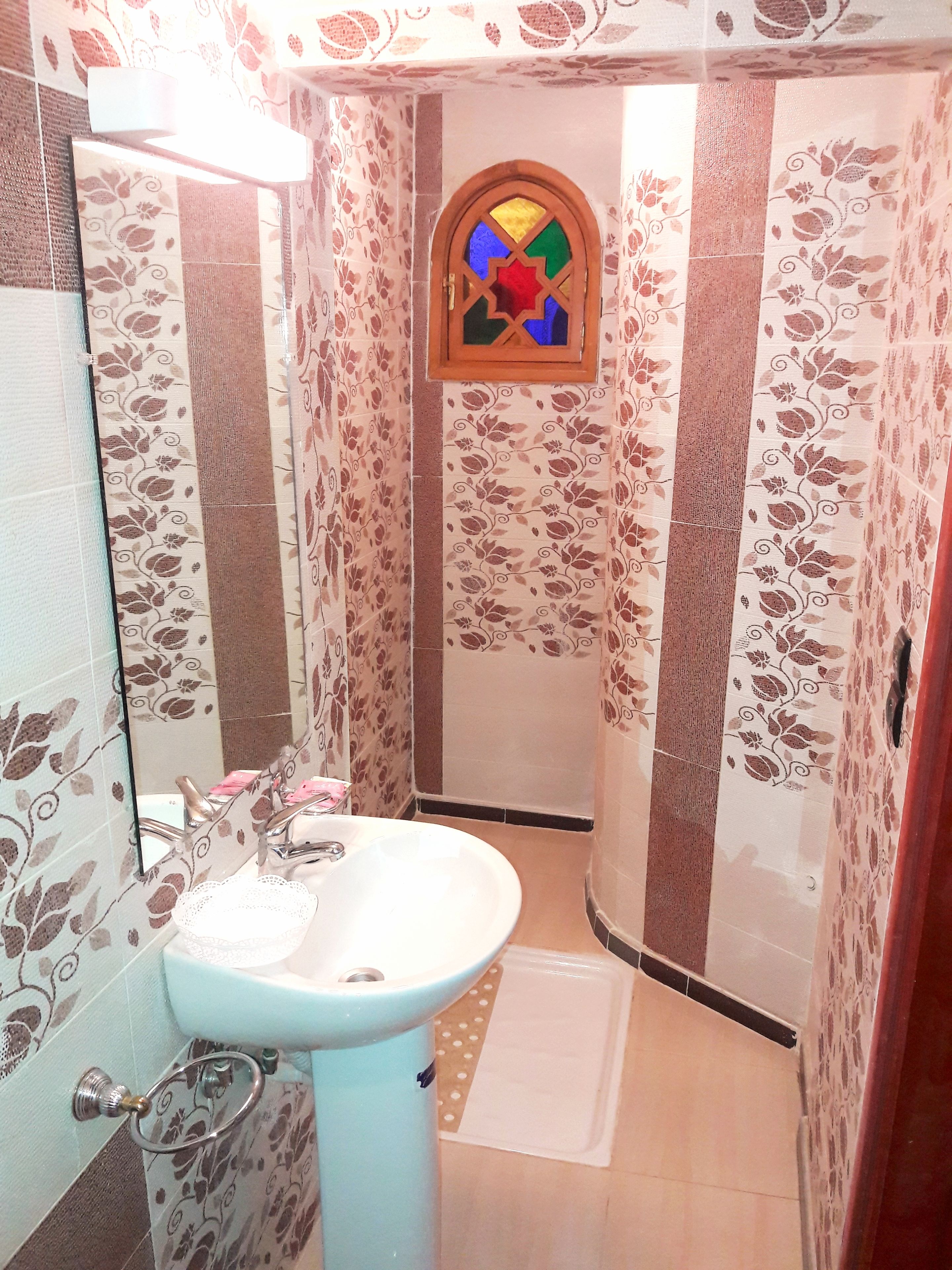 A bathroom with a white sink, a mirror, and a shower area with floral patterned walls.