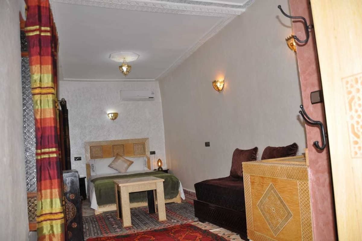 A room with a bed, a small table, a sofa, and two wall-mounted lights.