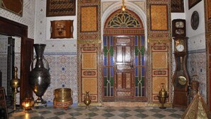 An ornate room with intricate tile work, a large wooden door with colorful patterns, and traditional furnishings including a large brass vase and a clock. - Riad Royal (Meknes)