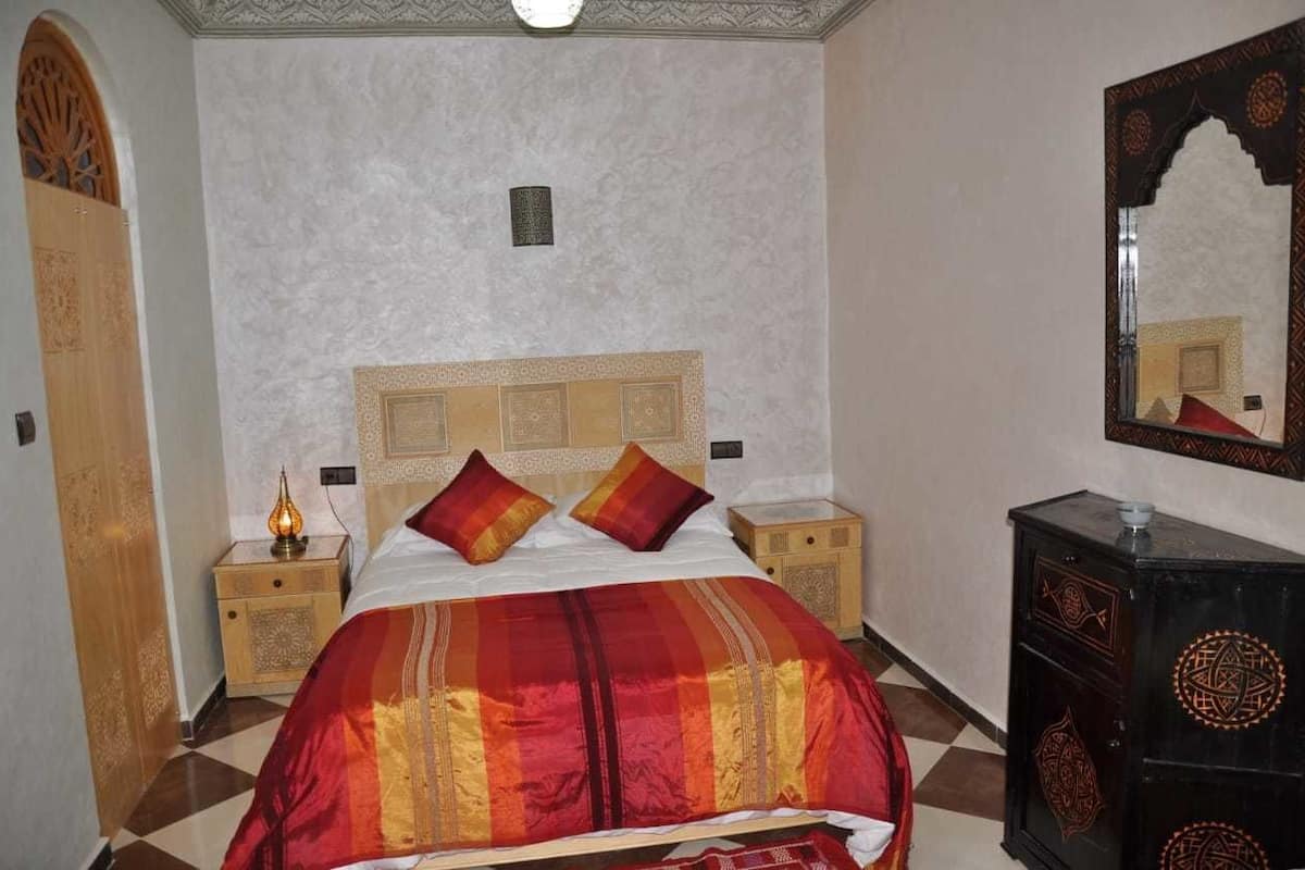 A bedroom with a large bed, two nightstands, a dresser, and a mirror.