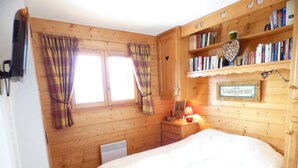 A wooden room with a bed, a nightstand, a shelf with books, and a window with curtains. - APARTMENT AT THE FOOT OF THE SLOPES (Villard-sur-Doron)