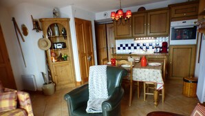 A cozy living room with a green armchair, a dining table with a red vase, and wooden cabinets. - APARTMENT AT THE FOOT OF THE SLOPES (Villard-sur-Doron)