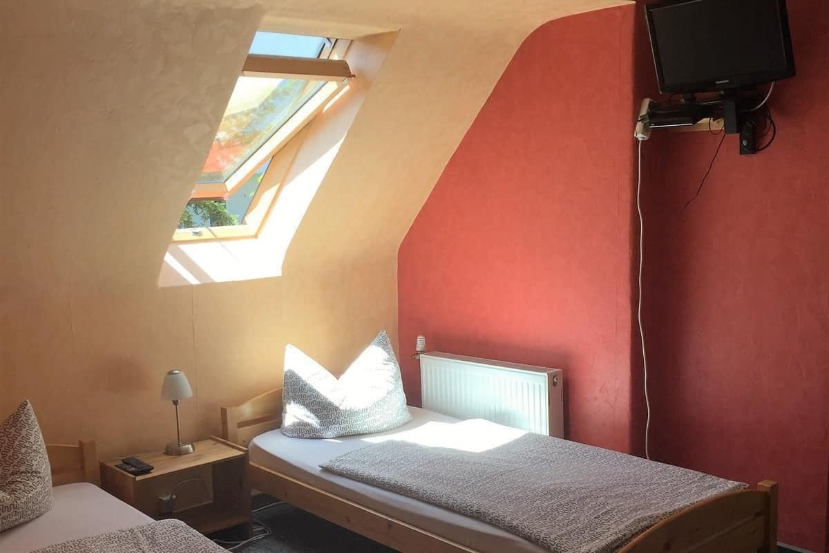 A room with two beds, a TV mounted on the wall, and a skylight.