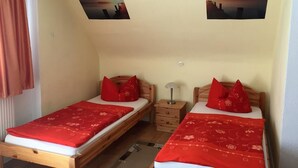 Una habitación con dos camas de madera, cada una con ropa de cama y almohadas rojas a juego. Hay dos mesitas de noche con lámparas, y las paredes están decoradas con dos cuadros enmarcados.