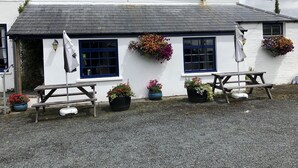 A white building with blue windows and a gravel ground. There are two wooden benches and potted plants. - Blue Lion Inn (Okehampton)