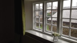 A window with a view of a brick building and a green curtain. - Blue Lion Inn (Okehampton)