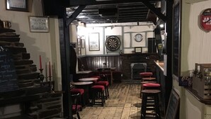 A cozy pub interior with wooden floors, red cushioned stools, and a dartboard on the wall. - Blue Lion Inn (Okehampton)
