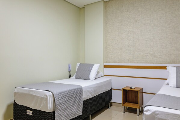 Una habitación de hotel con dos camas individuales, una mesita de noche de madera, un teléfono fijo en la pared y una pared de color claro.