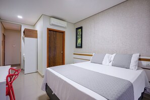 Ett hotellrum med en stor säng, en trädörr, en vit vägg med en inramad tavla och en röd stol.