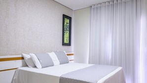 A neatly made bed with white bedding and gray pillows, a framed picture on the wall, and a window with white curtains. - OYO Tropical Confort Hotel, Brasilia (São Sebastião)