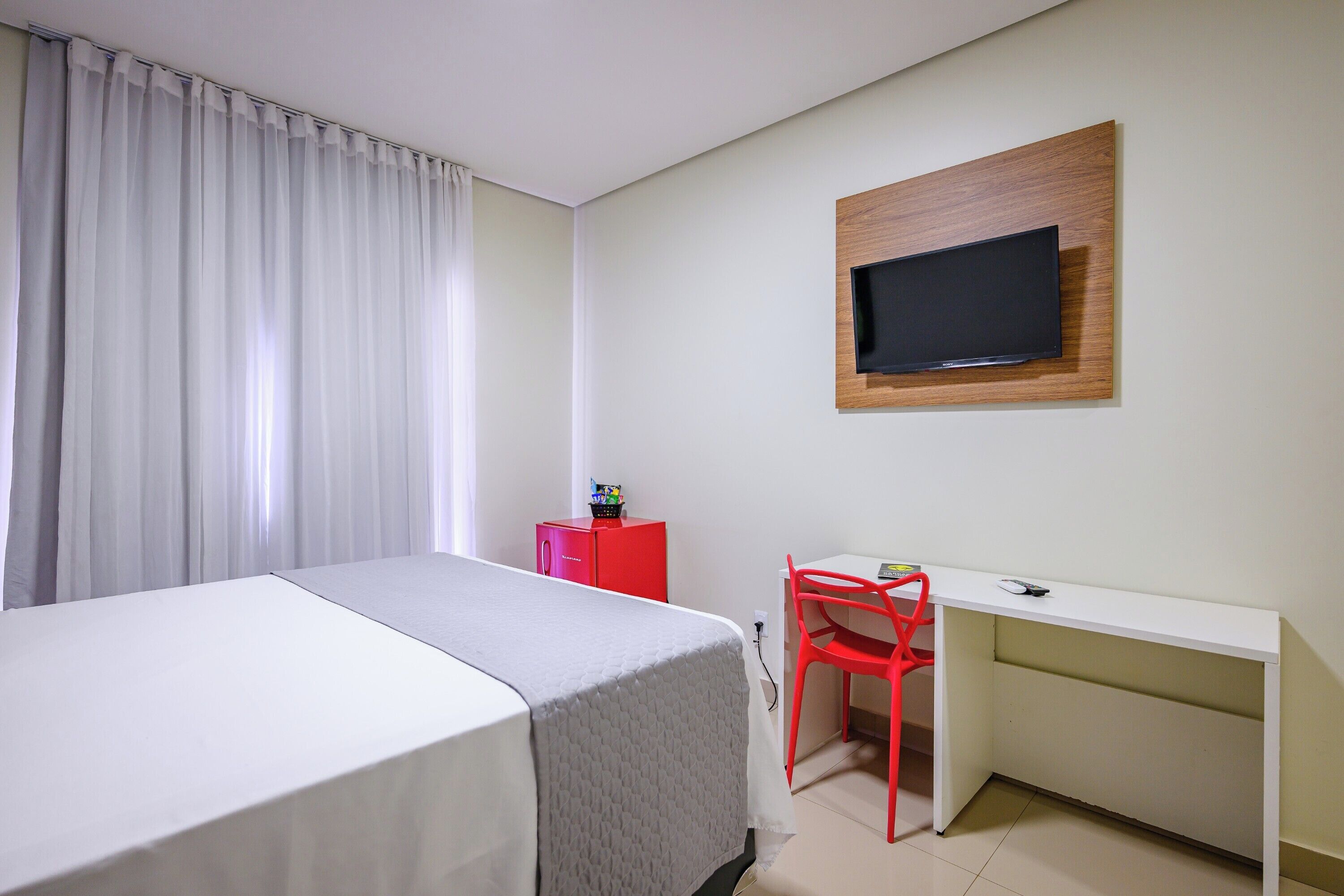 Hotellihuone, jossa on sänky, työpöytä, tuoli, seinälle asennettu televisio ja punainen kaappi.