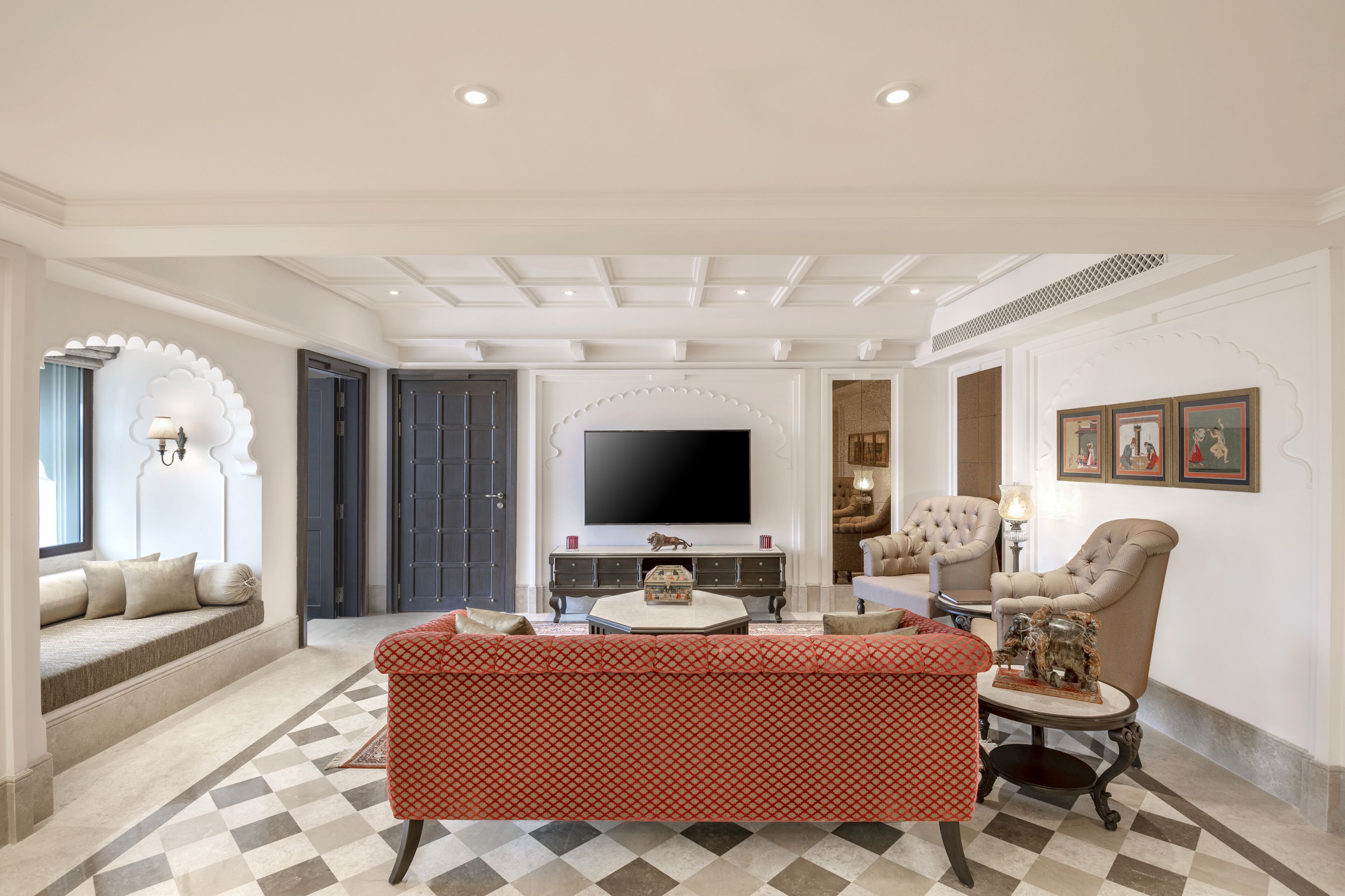 A spacious living room with a large flat-screen TV, a red patterned sofa, and a beige armchair.