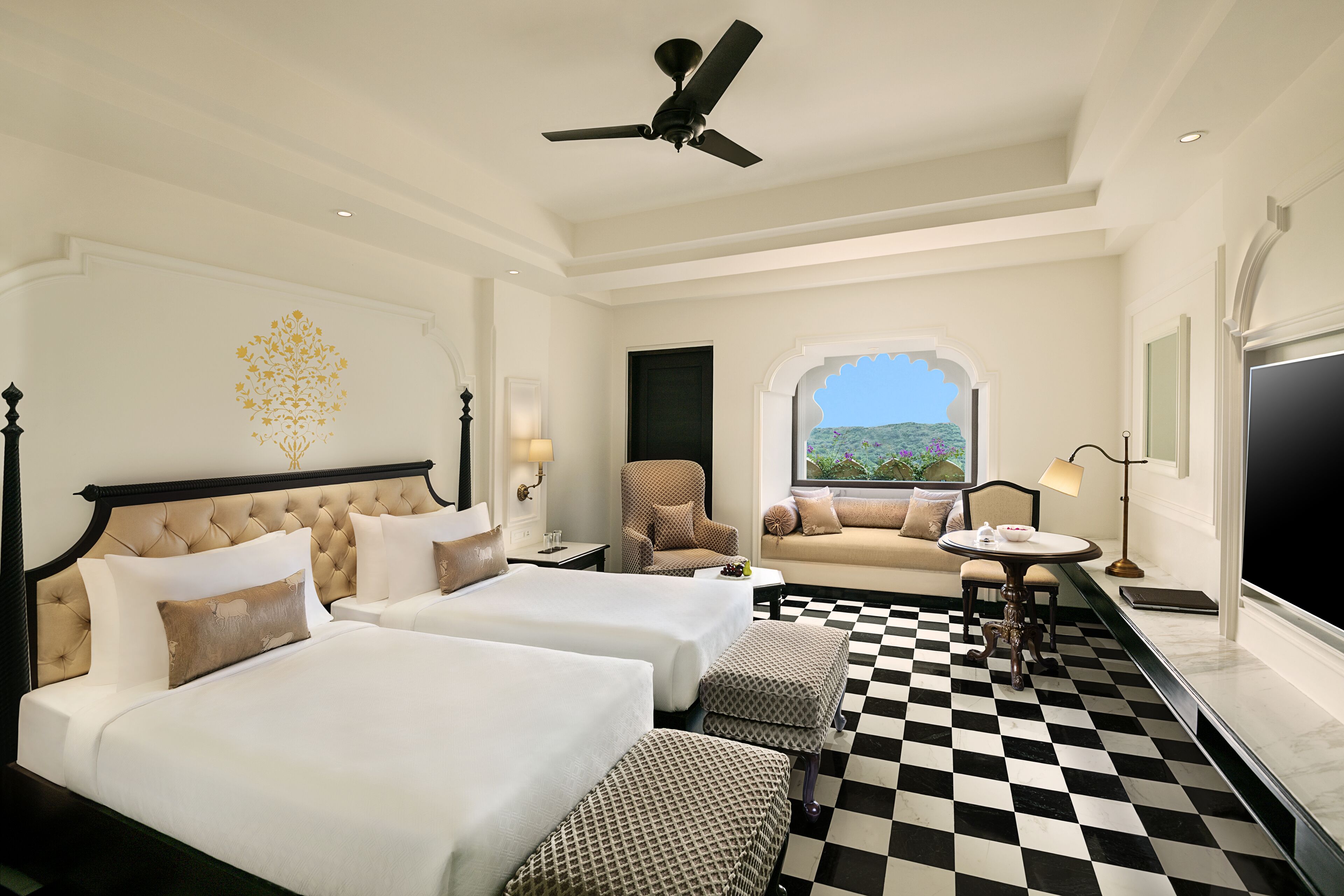 A hotel room with two beds, a sofa, a checkered floor, a ceiling fan, and a window with a view.
