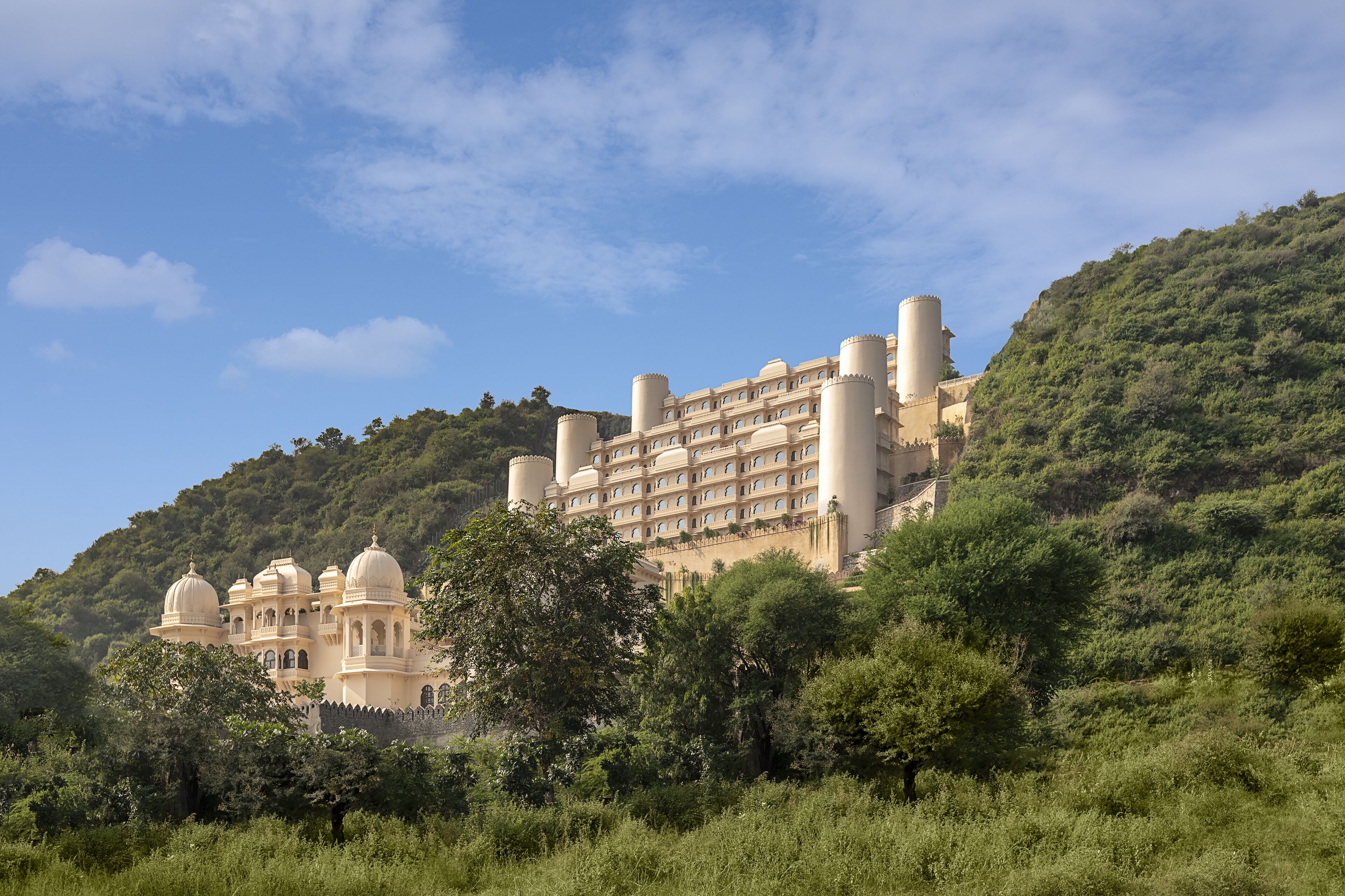 A large, multi-story building with a traditional architectural style, surrounded by lush greenery and hills.