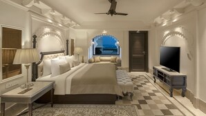 A hotel room with a large bed, a television, a desk, and a view of the city through a window. - Aurika, Udaipur - Luxury by Lemon Tree Hotels (Udaipur)